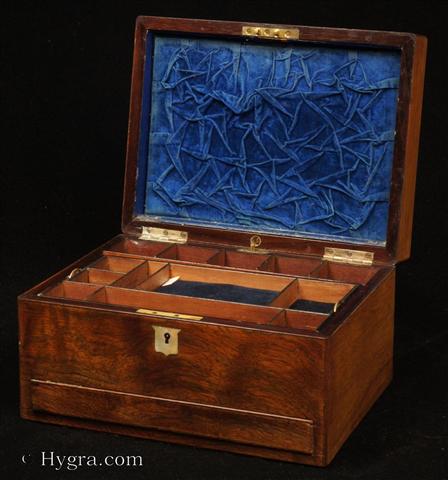 Antique Figured Rosewood box with lift-out compartmentalized tray and sprung drawer fitted for jewelry. There are mother of pearl escutcheons to the top and the front. There is a ruched velvet pad in the lid with mirror framed with gold embossed leather  behind.  It is released by pressing behind the lock catch. The sprung drawer is released by pressing on a button in the centre of the back facing. The lift-out tray  is of mahogany construction with rosewood facings. New pads of velvet have been made to make the tray suitable for jewelry. There is further space beneath. Circa 1850. -Enlarge Picture